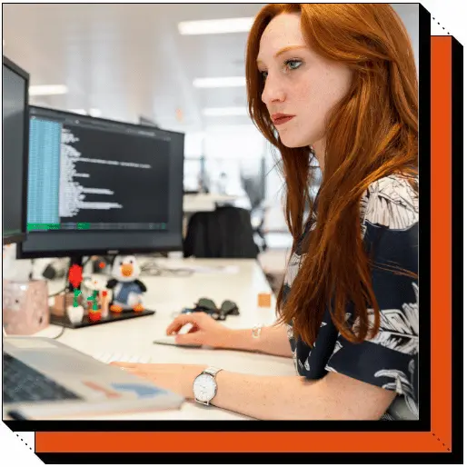 Female software developer working at her desk with multiple monitors displaying code.