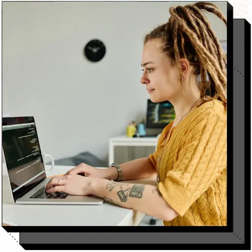 Female programmer with dreadlocks and tattoos, coding on a laptop in a modern workspace."
