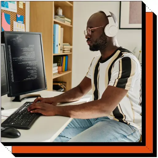 Male software developer wearing headphones, coding on a dual-monitor setup in a home office.
